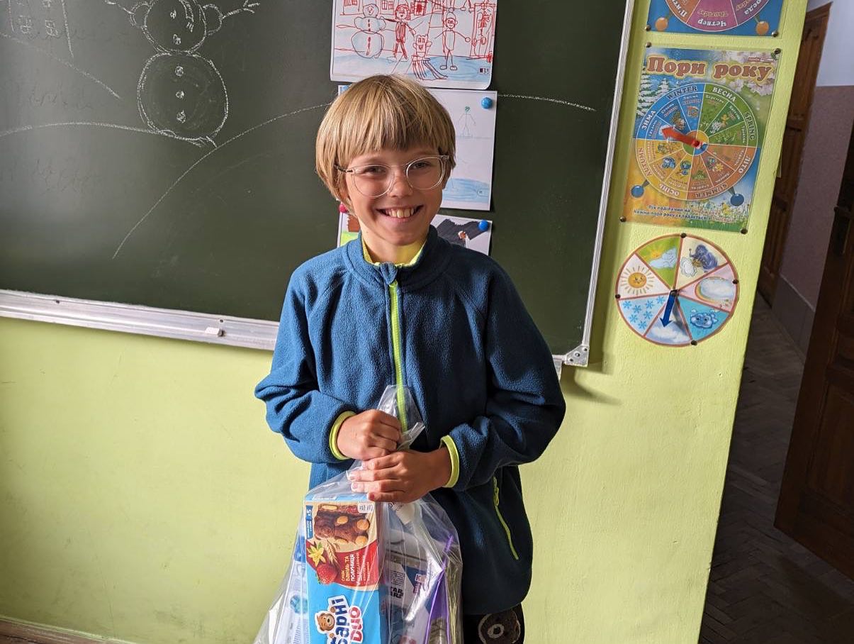A young boy holding a bag of toys in front of a blackboard.