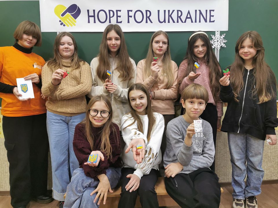 A group of young people posing in front of a sign that says hope for ukraine.