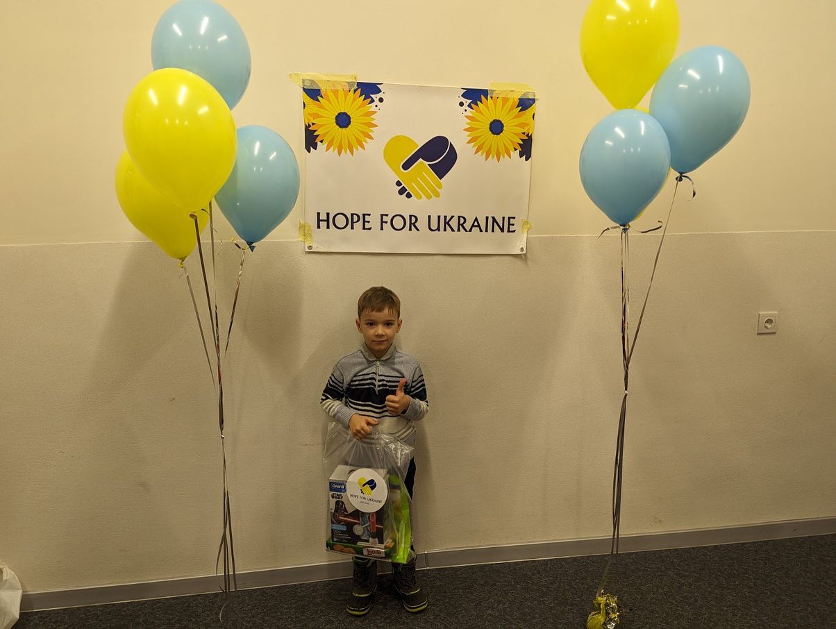 A boy standing in front of balloons and a sign that says hope for ukraine.