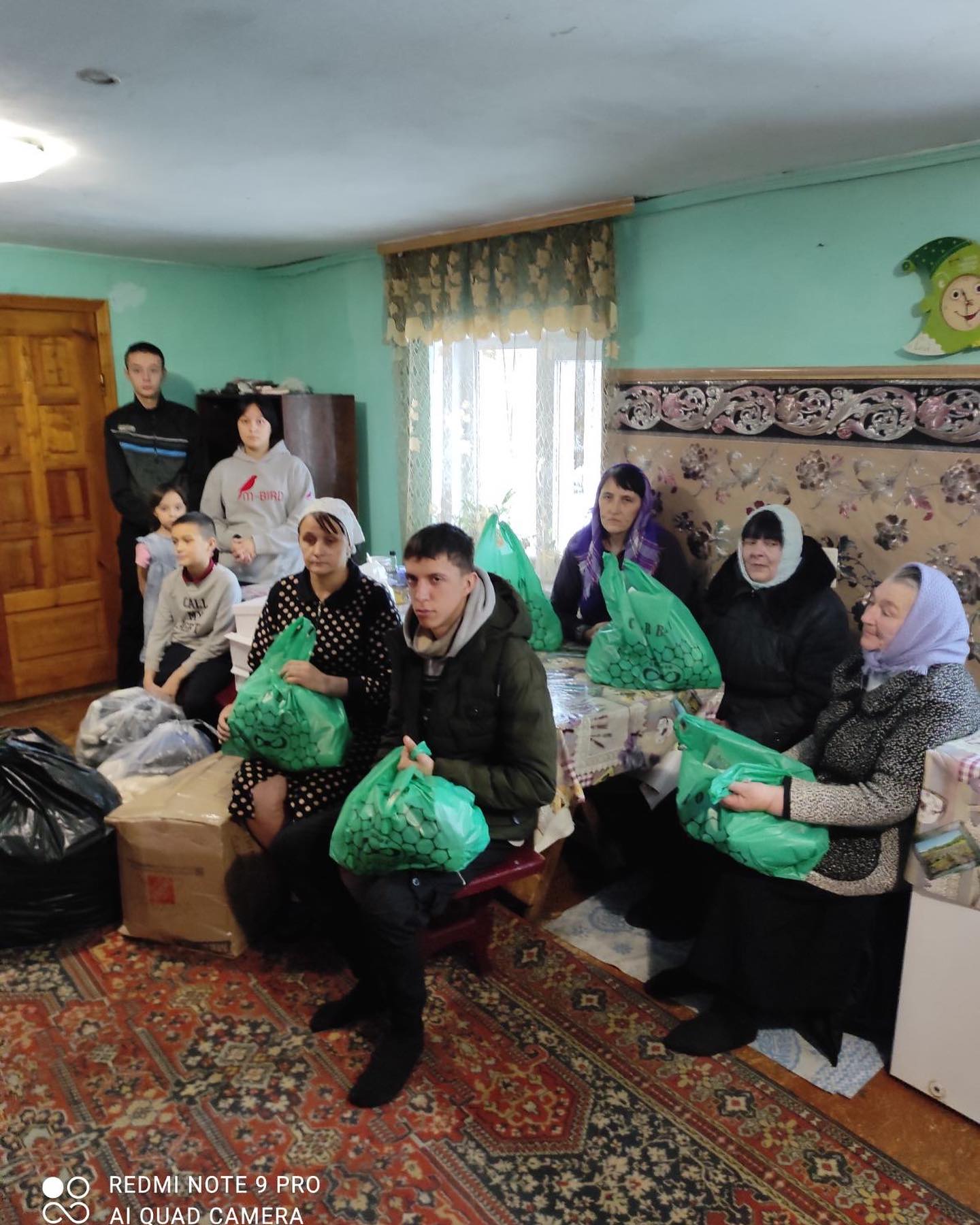 A group of people sitting in a room with green bags.