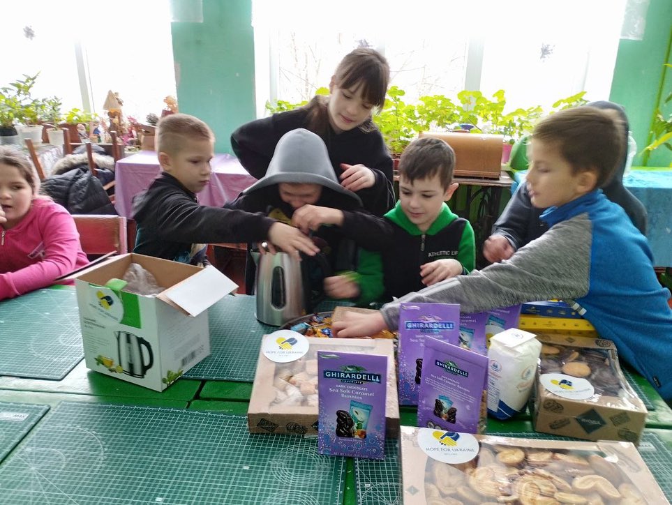 A group of children are sitting around a table with boxes.