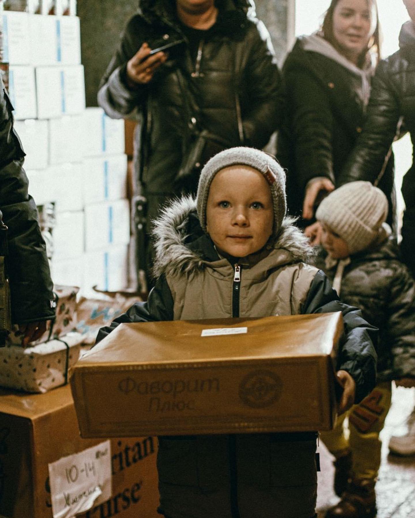 A young boy holding a box in front of a group of people.