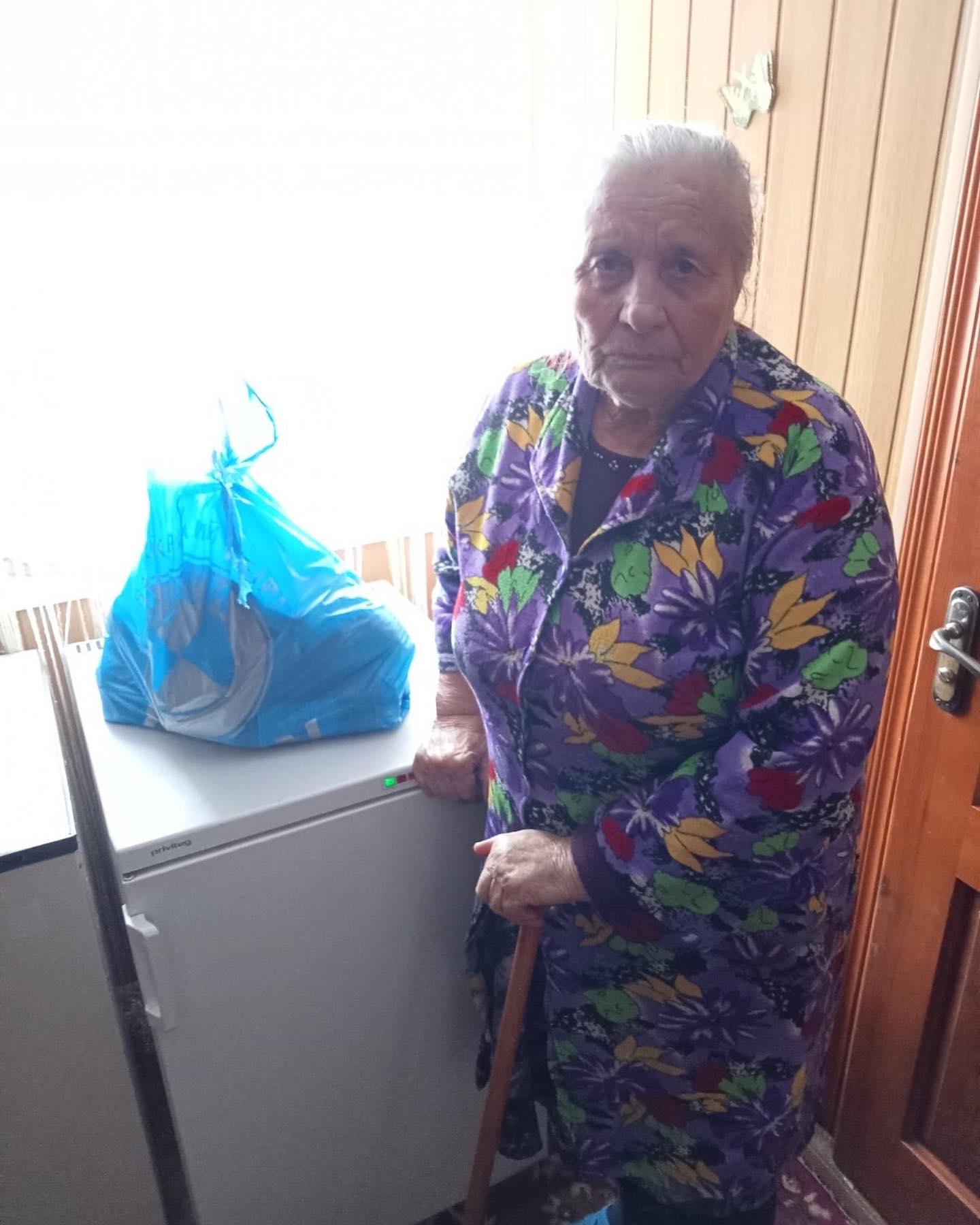 A woman with a cane standing next to a refrigerator.