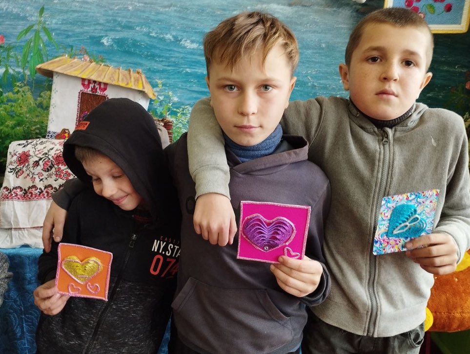Three boys holding up cards with hearts on them.