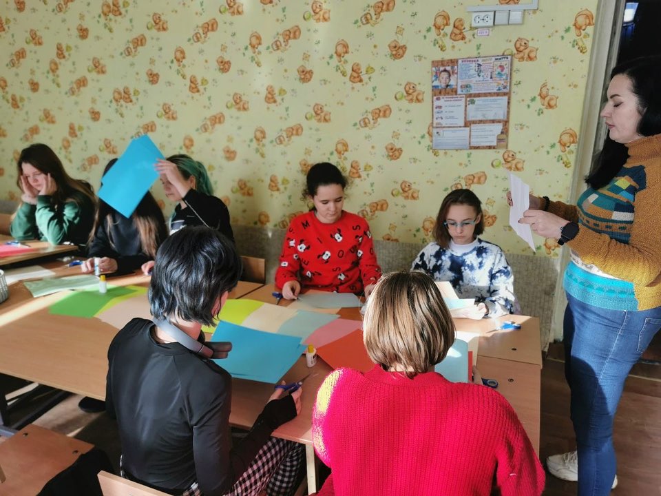 A group of people sitting around a table with colored paper.