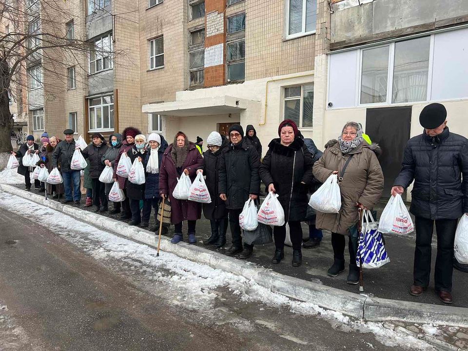 A group of people standing on a street with bags of food.