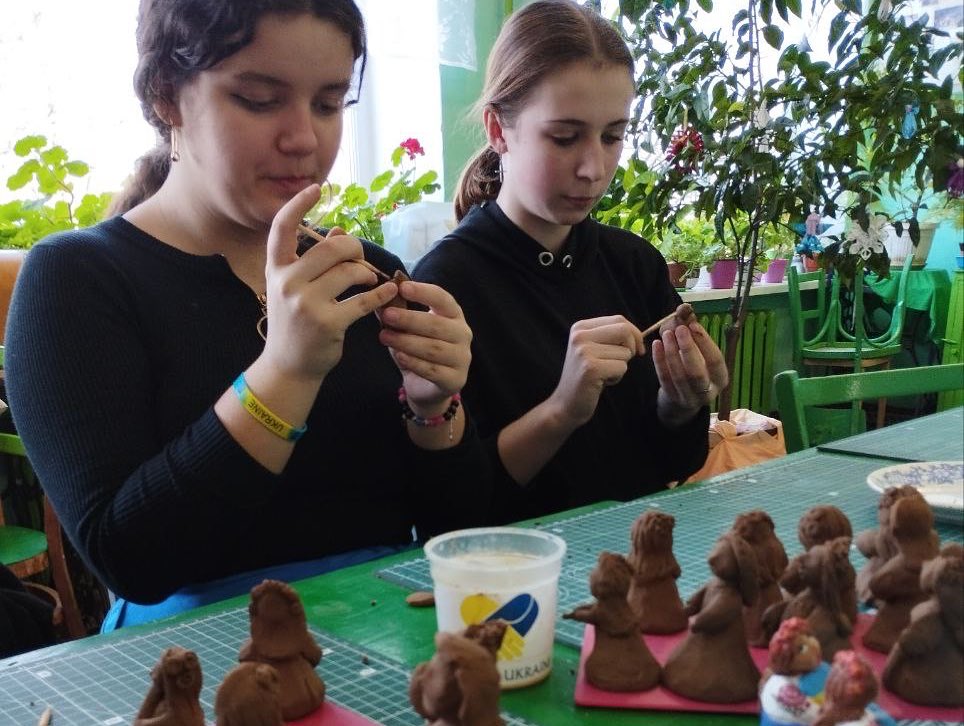 Two individuals shaping clay figures at a crafting table.