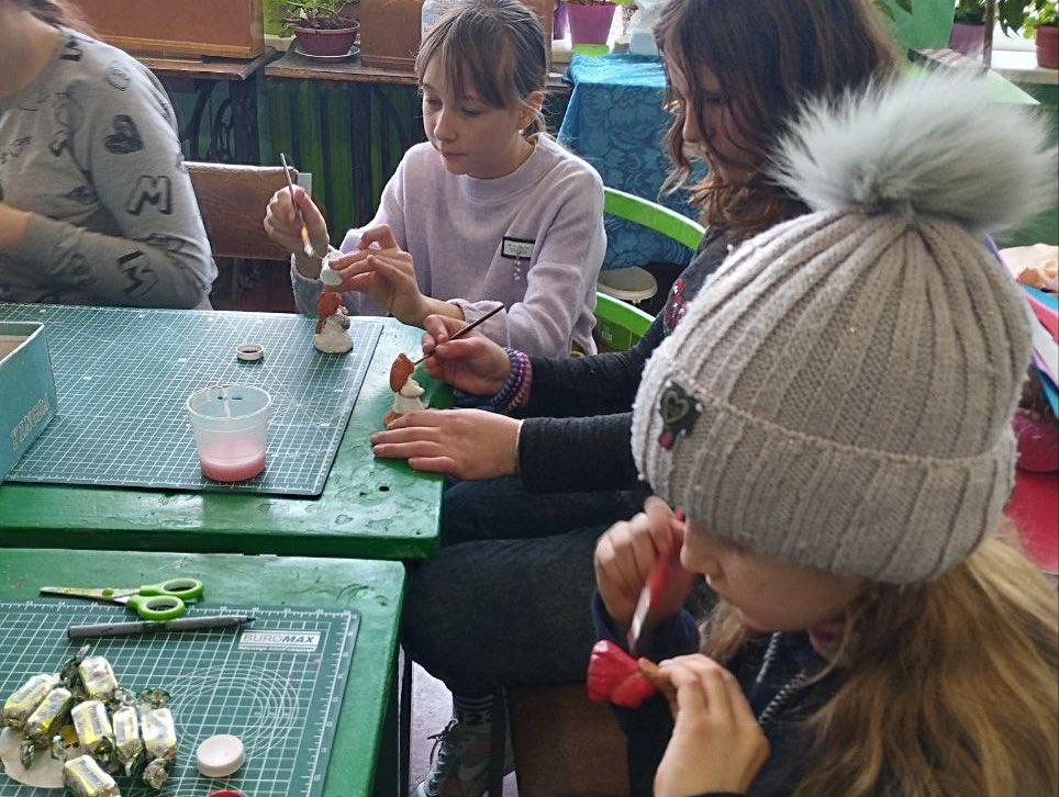 Children engaged in a craft activity, making objects from colorful materials at a table.