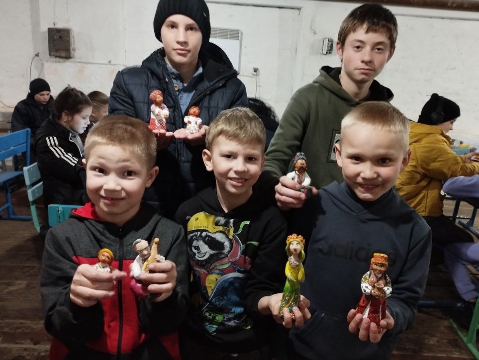Four boys displaying handmade figurines indoors.