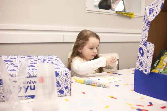 A young child focusing intently on a painting activity at a table with art supplies.