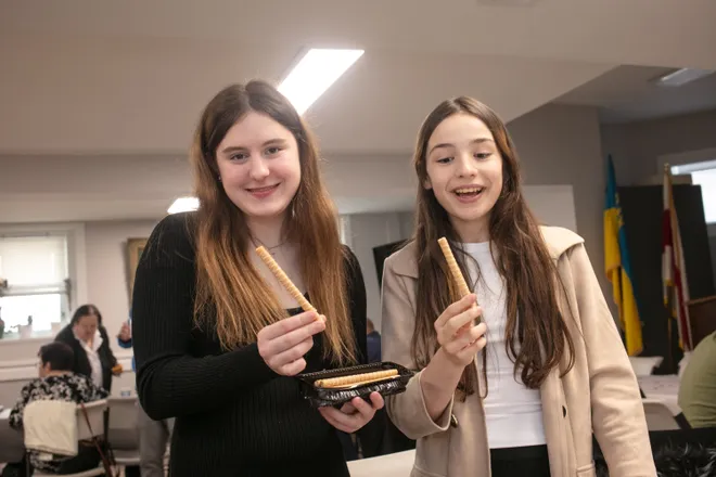 Two smiling young women holding breadsticks at a social gathering.