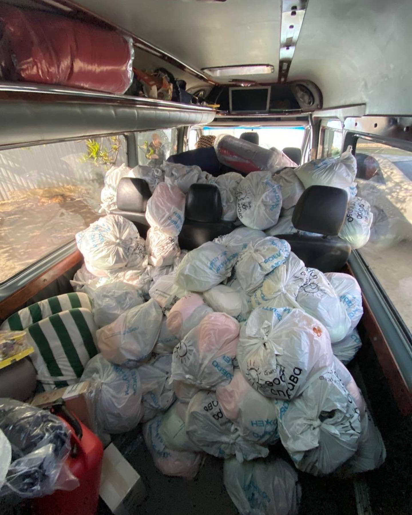 Interior of a van filled with numerous plastic bags containing humanitarian aid for Ukraine, with visible front seats and van ceiling.