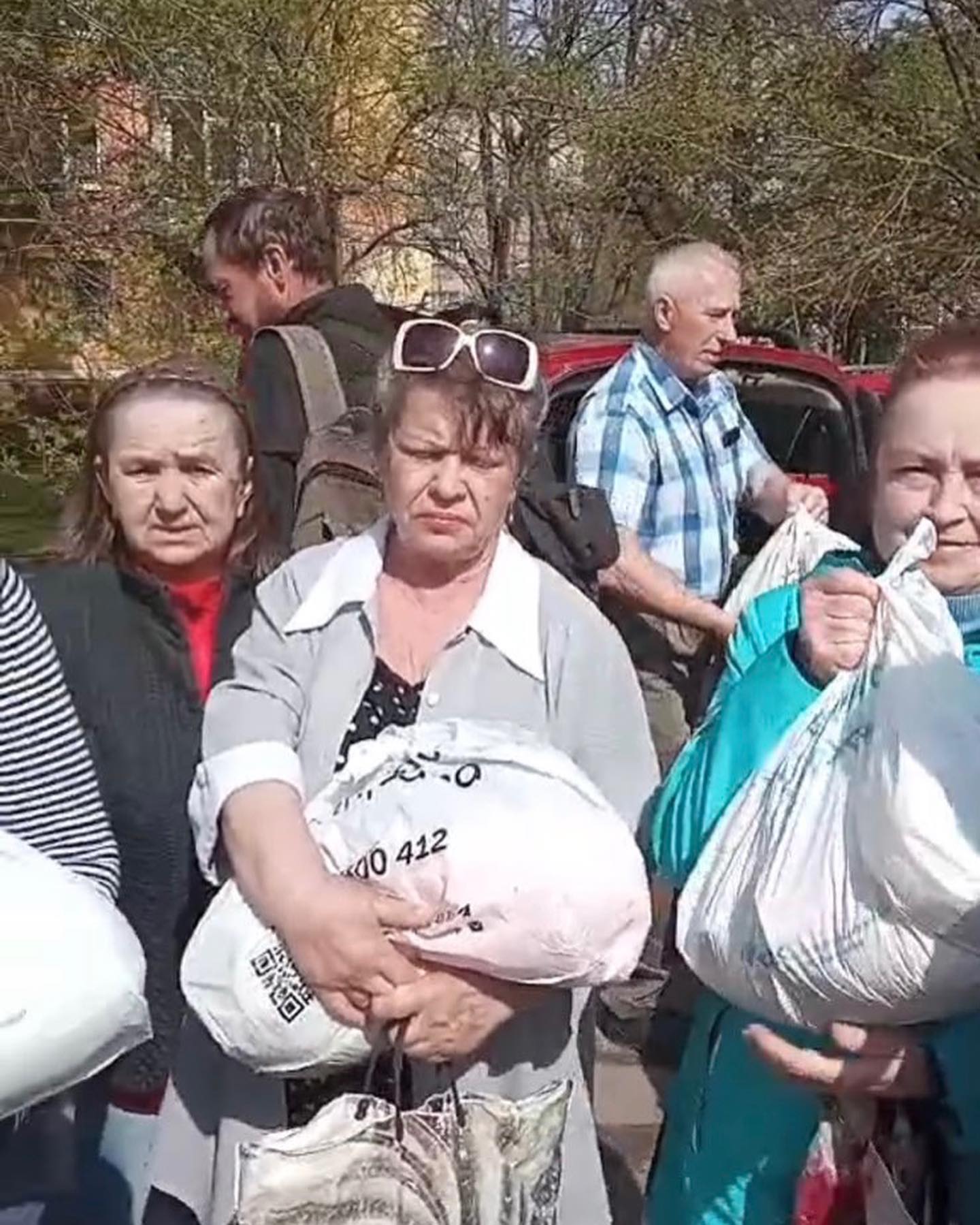 People holding bags and supplies, standing by a vehicle in a sunny outdoor setting, ready to volunteer help for Ukraine.