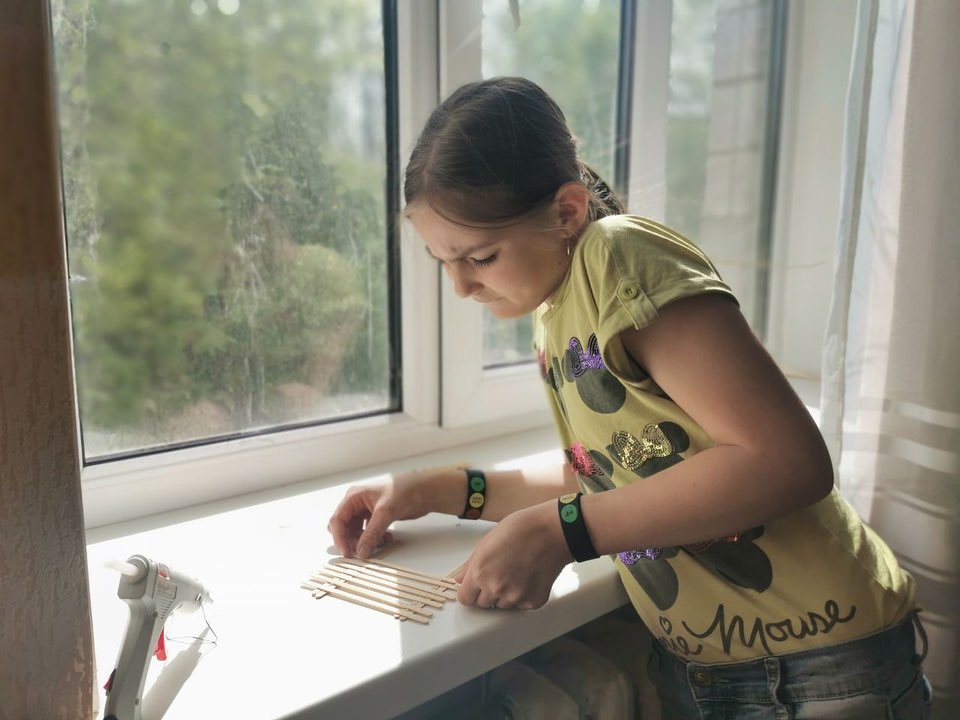Young girl concentrating on arranging sticks on a lit table by a window in the Donetsk region.