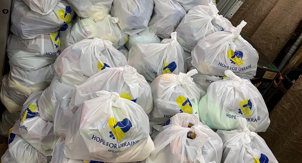 Plastic bags filled with food aid, labeled "Hope for Ukraine," stacked in a distribution area.