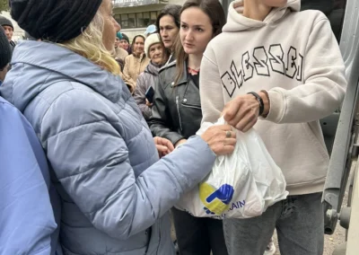 People receive aid bags labeled "Ukraine" from a vehicle while standing in a crowded outdoor line.