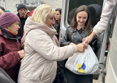 A group of people receives bags of supplies from a person standing in a van, with several individuals waiting in line outdoors.
