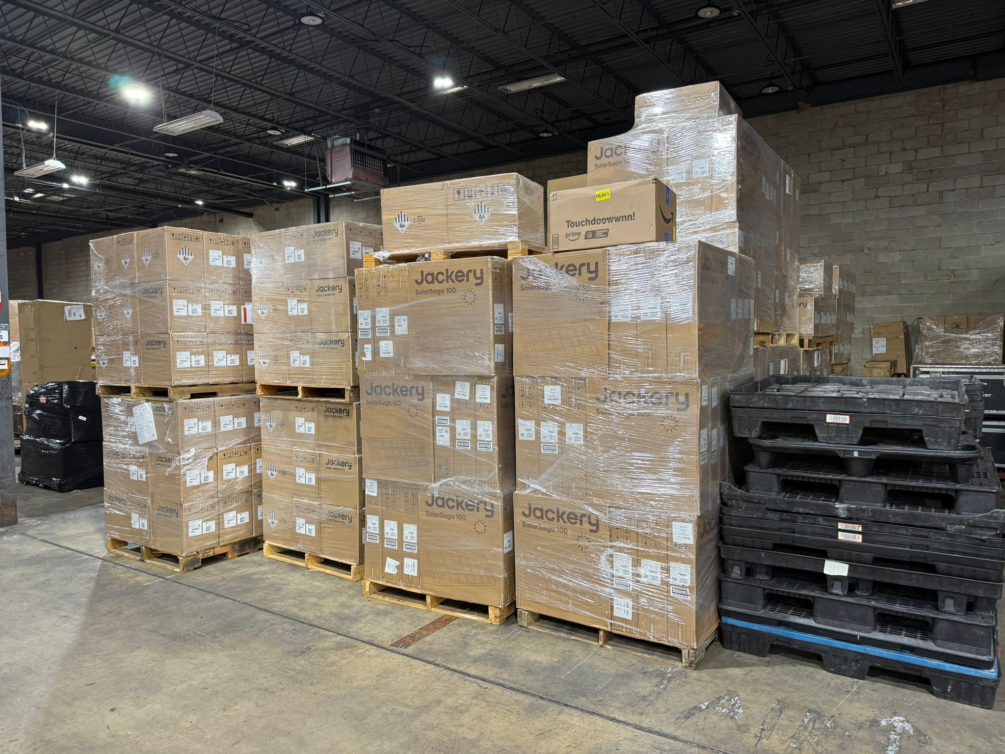 Stacks of large cardboard boxes labeled "Jackery" are shrink-wrapped on pallets in a warehouse, reminiscent of humanitarian aid efforts for Childhood Interrupted in Ukraine, with black plastic pallets stacked nearby.