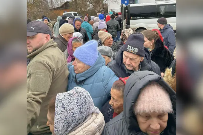 A group of elderly people wearing winter clothing gather closely together outdoors near a vehicle, finding heat in hunger as they share warmth and companionship on a cold day.
