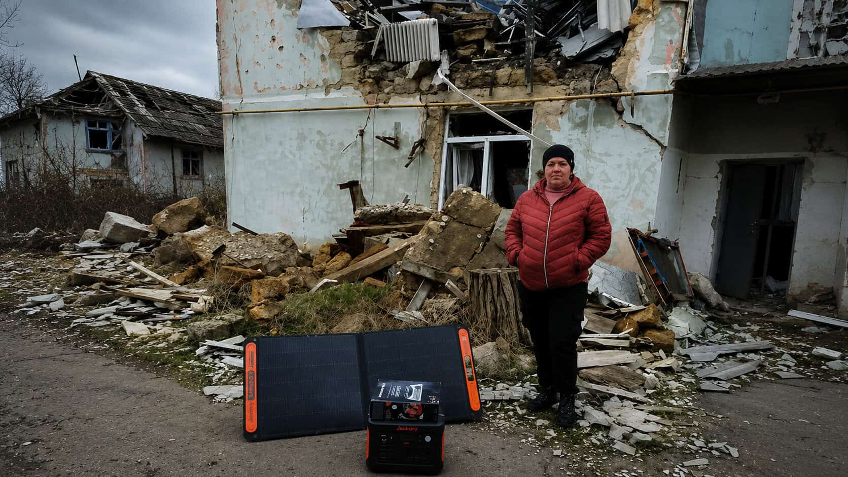Ukrainian woman stands in a street with destroyed building behind and a jackery solar kit provided by Hope for Ukraine