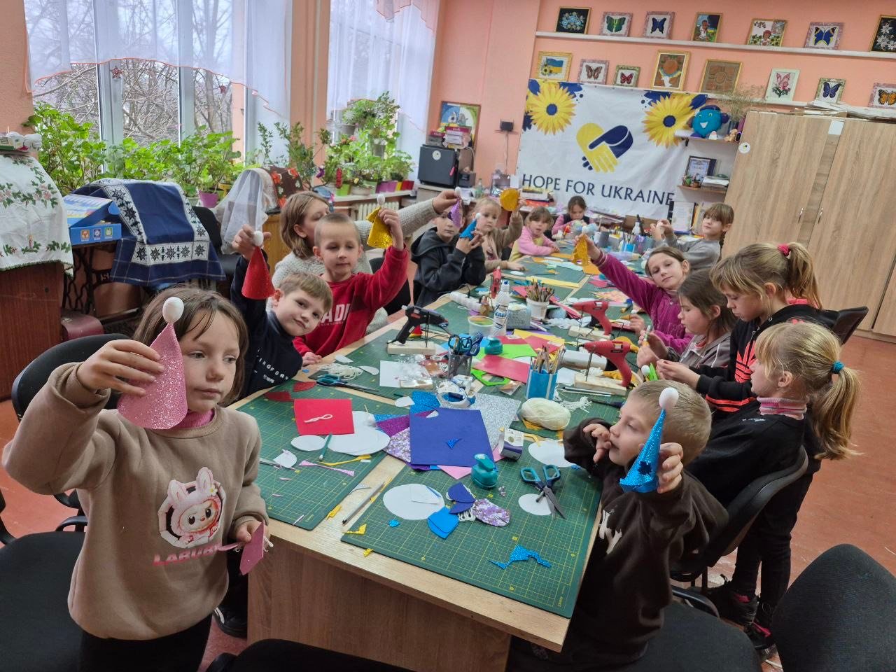 A group of children sit around tables doing arts and crafts in a classroom decorated with Ukrainian flags and a “Hope for Ukraine” banner, offering support amid the Ukrainian children mental health crisis.