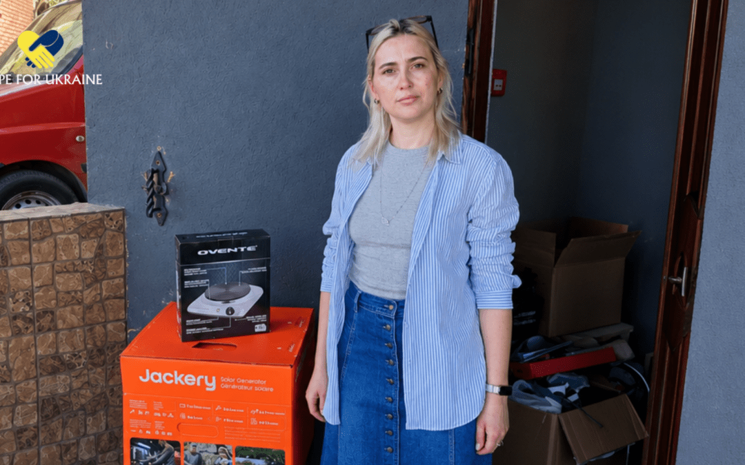 A Ukrainian woman standing in her doorway beside a Jackery solar generator and portable cooktop delivered by Hope For Ukraine.