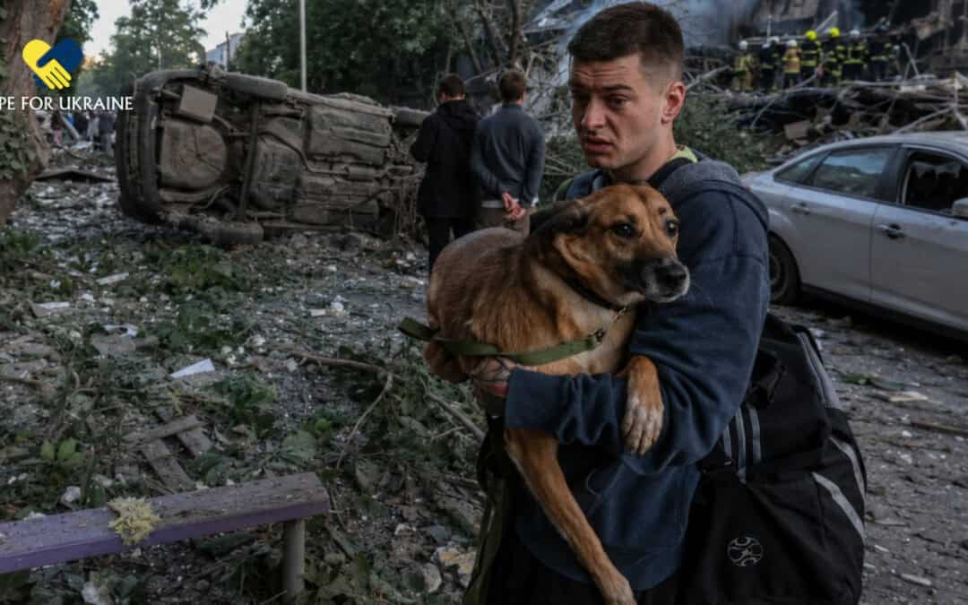 A man carries a frightened dog through smoke, rubble, and debris after an attack in Ukraine.