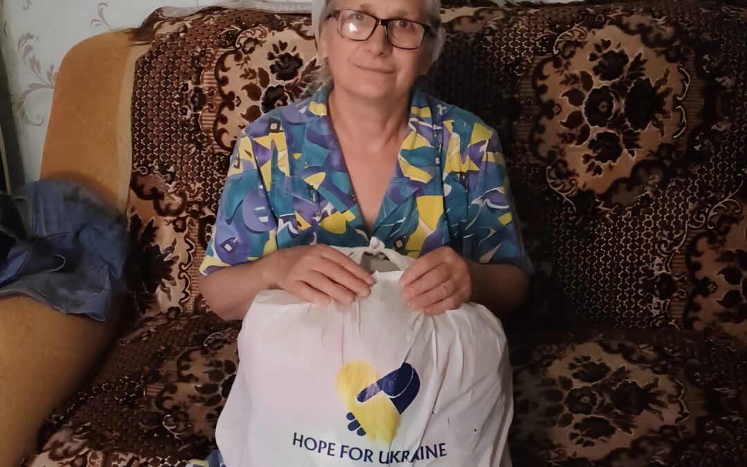 Woman in Ukraine holding a Hope For Ukraine food assistance bag while seated in her home.