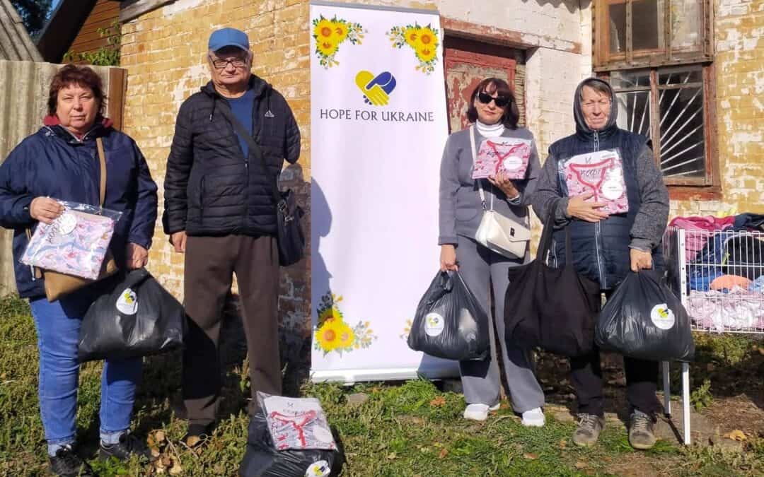 Four people holding aid packages in front of a Hope For Ukraine banner.