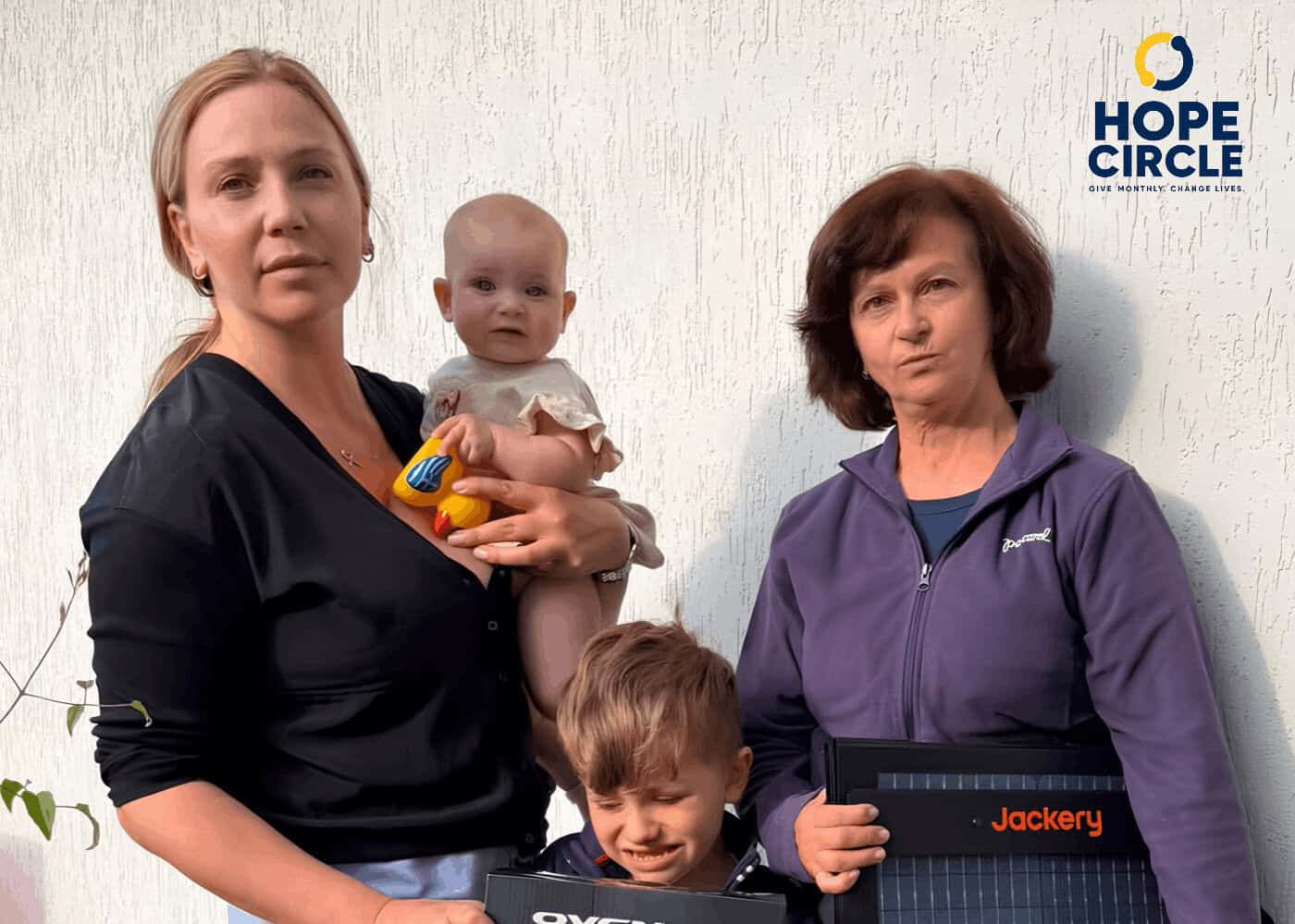A woman holding a baby and a young boy stands next to a second woman holding a solar panel, with the Hope Circle logo in the corner.